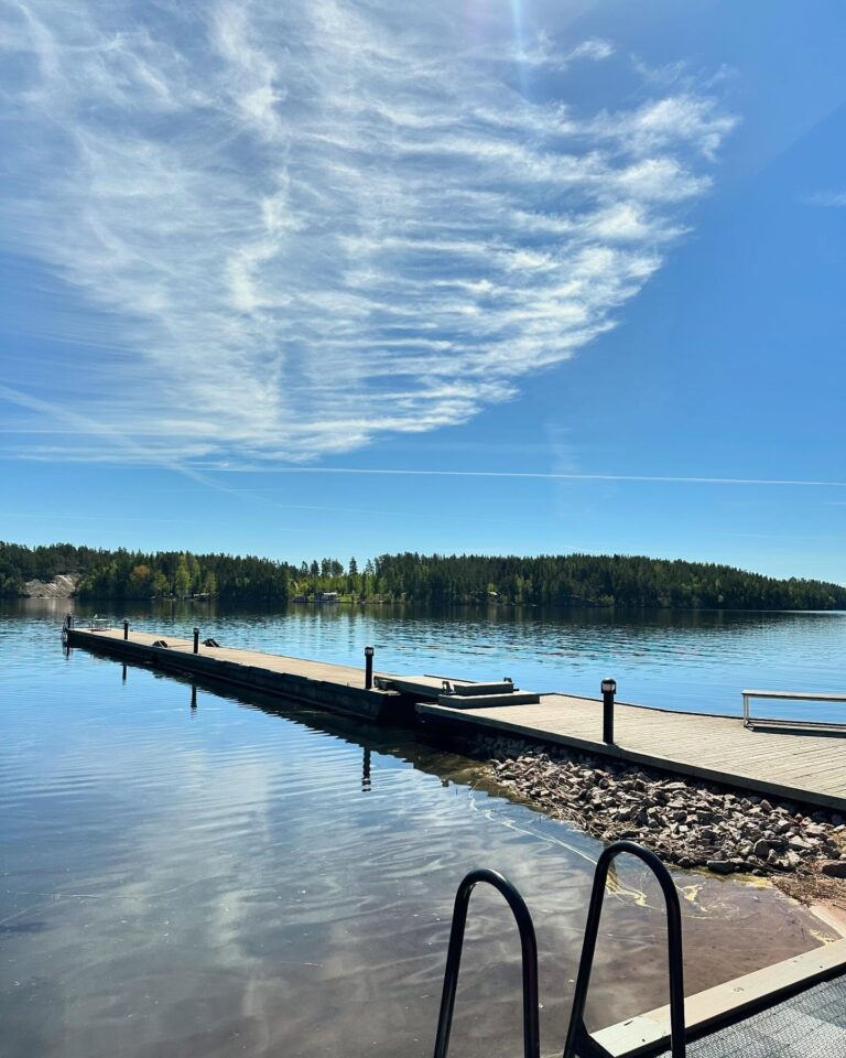 Lång träbrygga ut i spegelblanka Sommen under högblå himmel