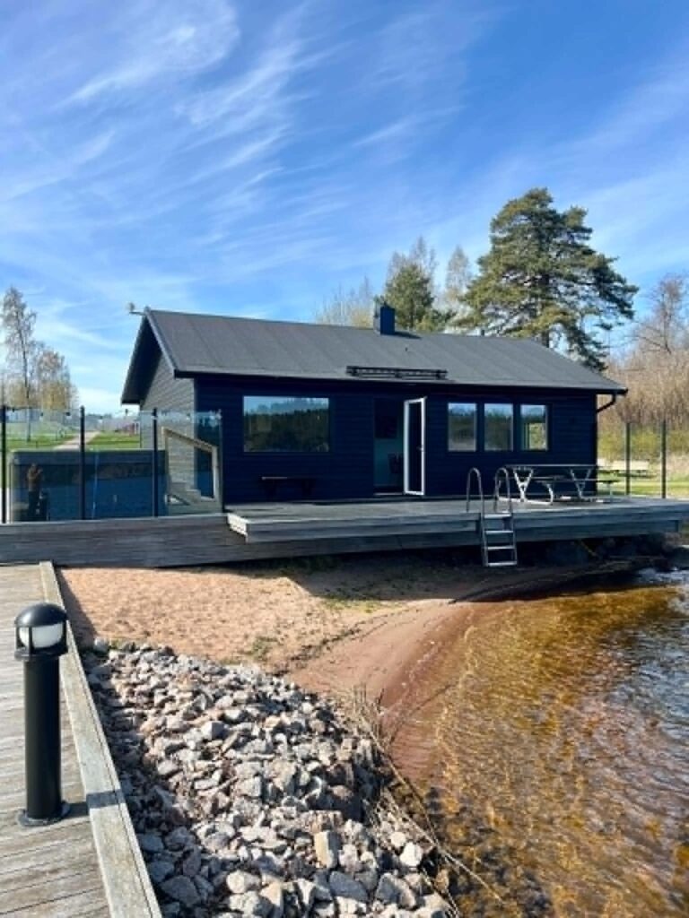 Bastuhus i svart trä med altan och badstege vid sandstranden