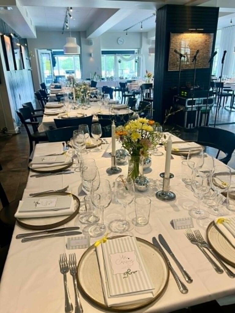 Långbord dukat med guldunderlägg, menykort, ljusstakar och sommarblommor