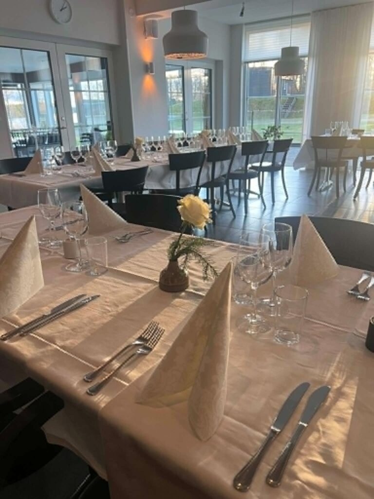 Dukade bord med vita servetter, kristallglas och en gul ros i eftermiddagssol