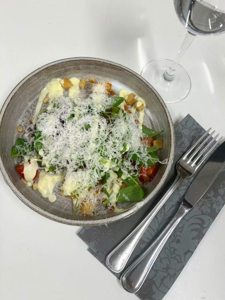 Caesarsallad med riven parmesan, krutonger och tomat i keramikskål vid dukat bord
