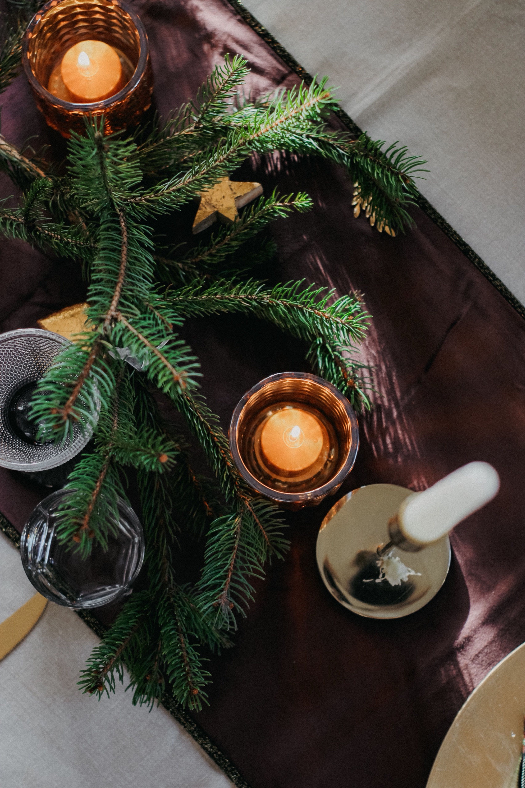 Julbordsdukning ovanifrån med värmeljus, granris och glas på mörk löpare