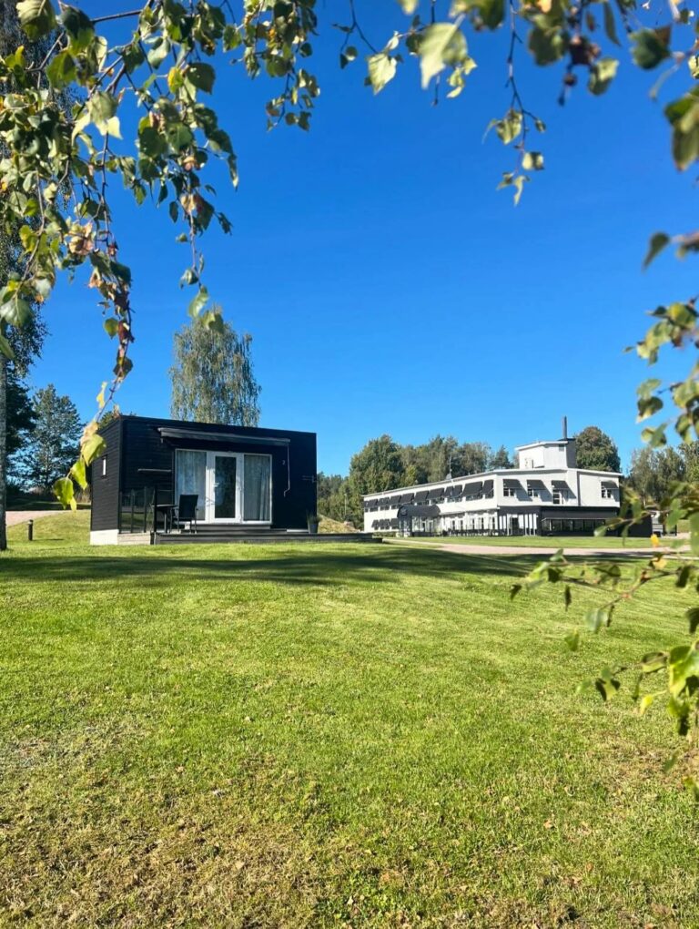 Hotellbyggnaden och en av stugorna sedda över gräsmattan mellan björkar