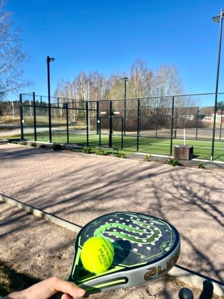 Padelracket och boll framför utomhusbanan en solig dag