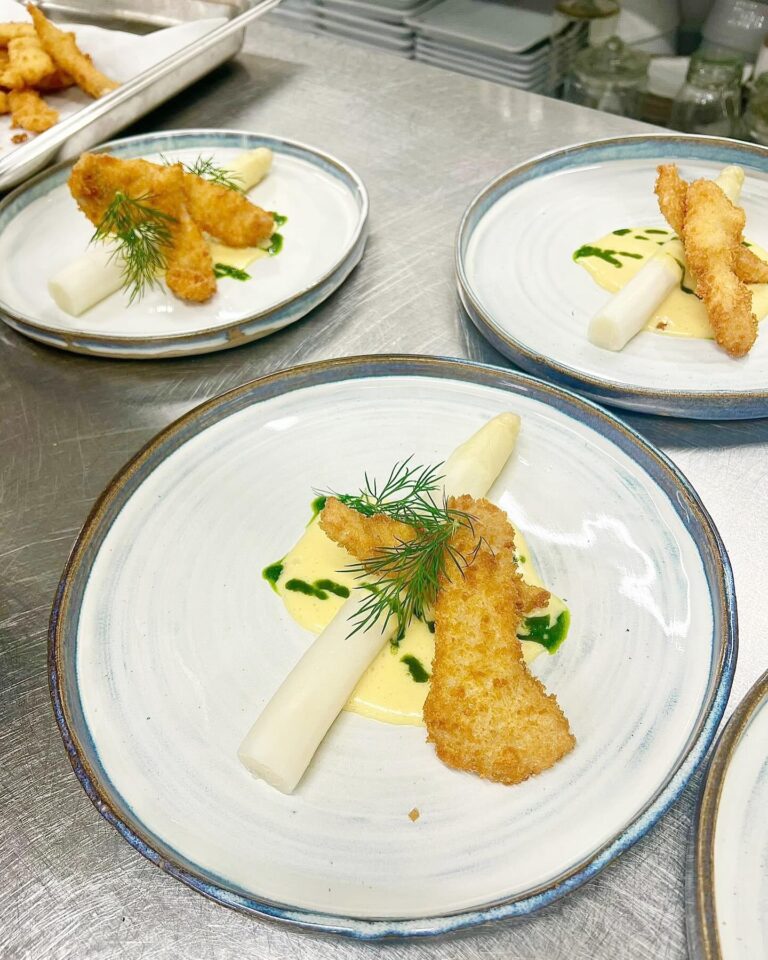 Friterad abborre med hel vit sparris, hollandaise och dillkvist på keramiktallrik