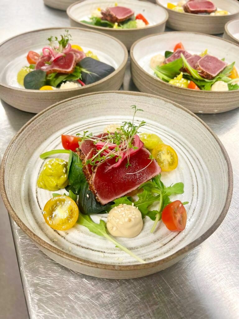 Tonfiskskivor på salladsblad med tomater i olika färger och avokadokräm